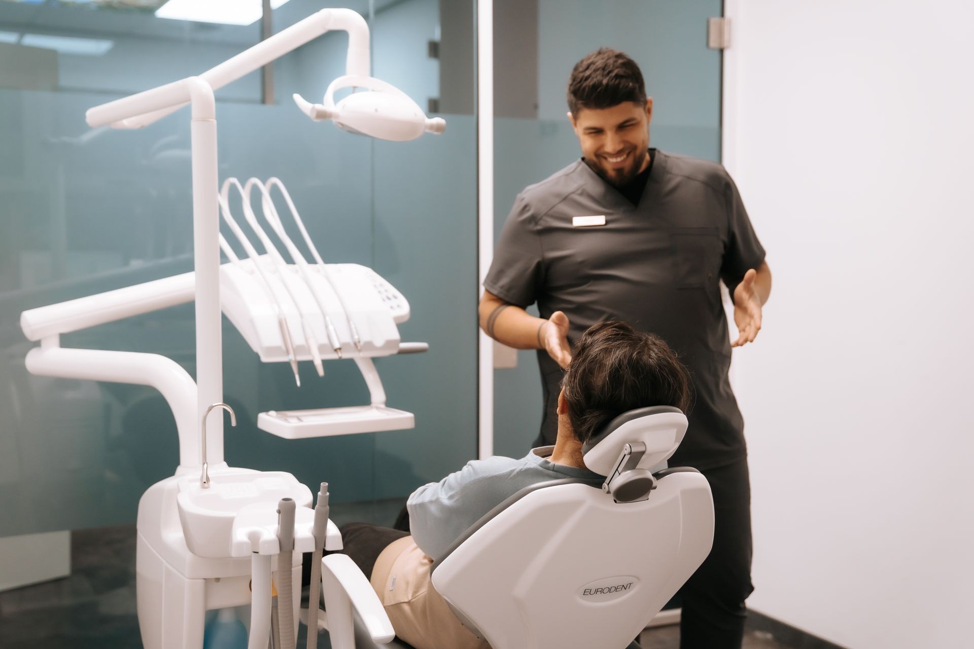 Dentist talking to a patient seated in a dental chair with dental equipment in the foreground.