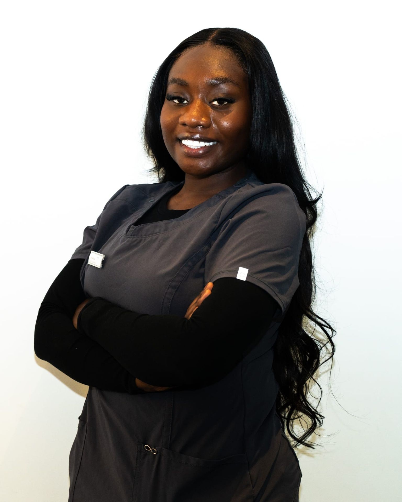 Person wearing gray scrubs with long hair, arms crossed over chest against a plain white background.