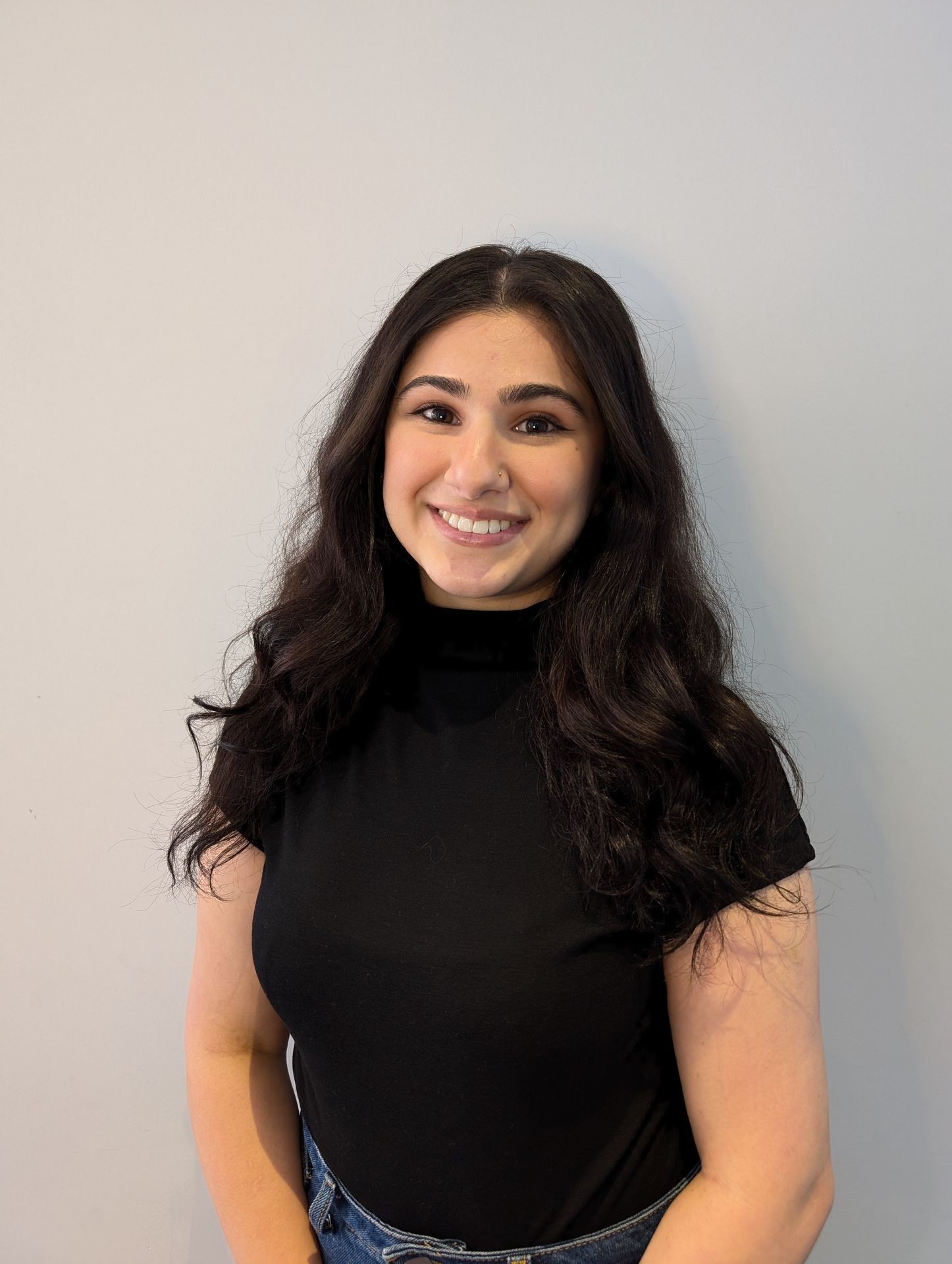 Smiling person with long dark hair wearing a black shirt against a neutral background.