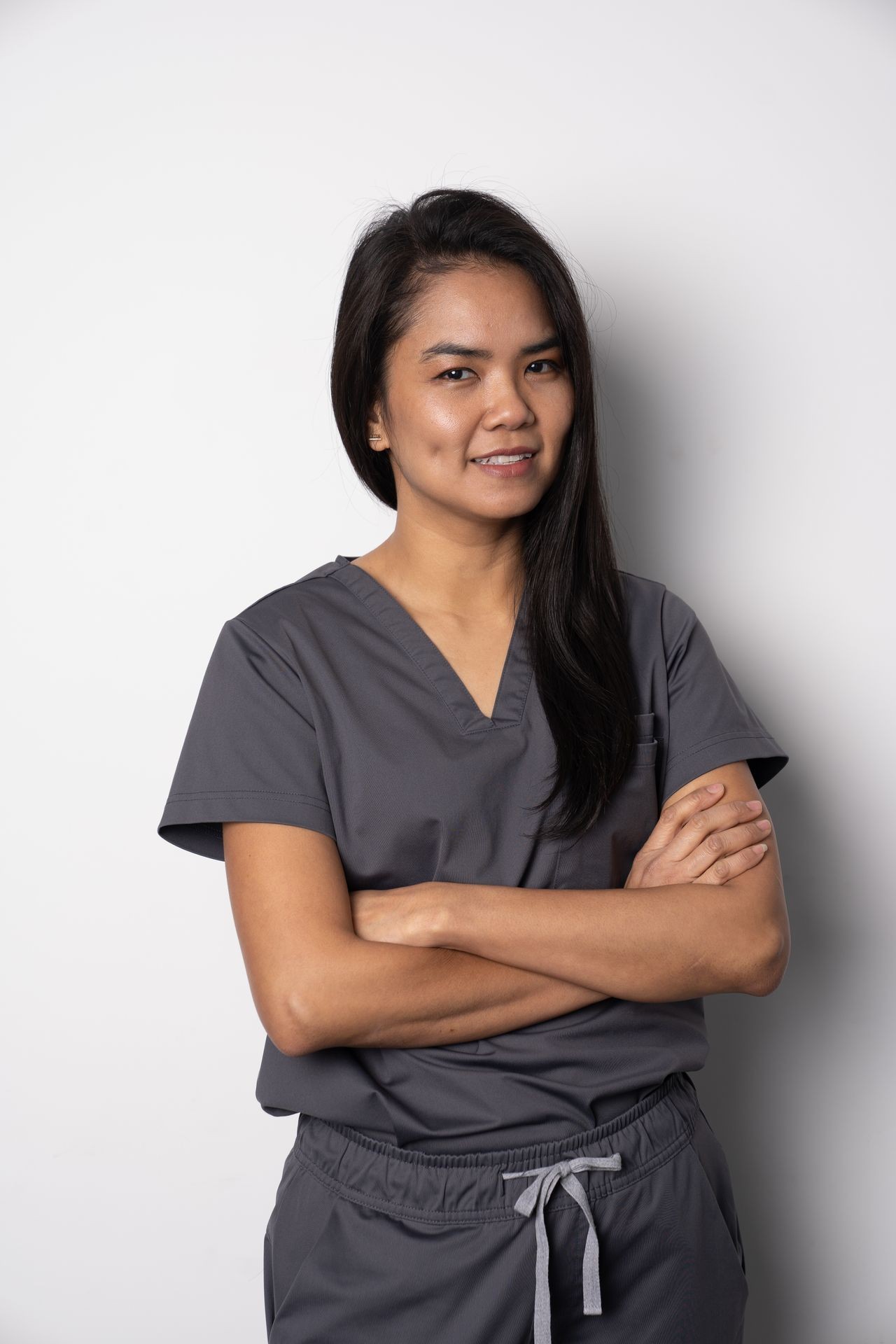 Person wearing gray medical scrubs with arms crossed, standing against a white background.