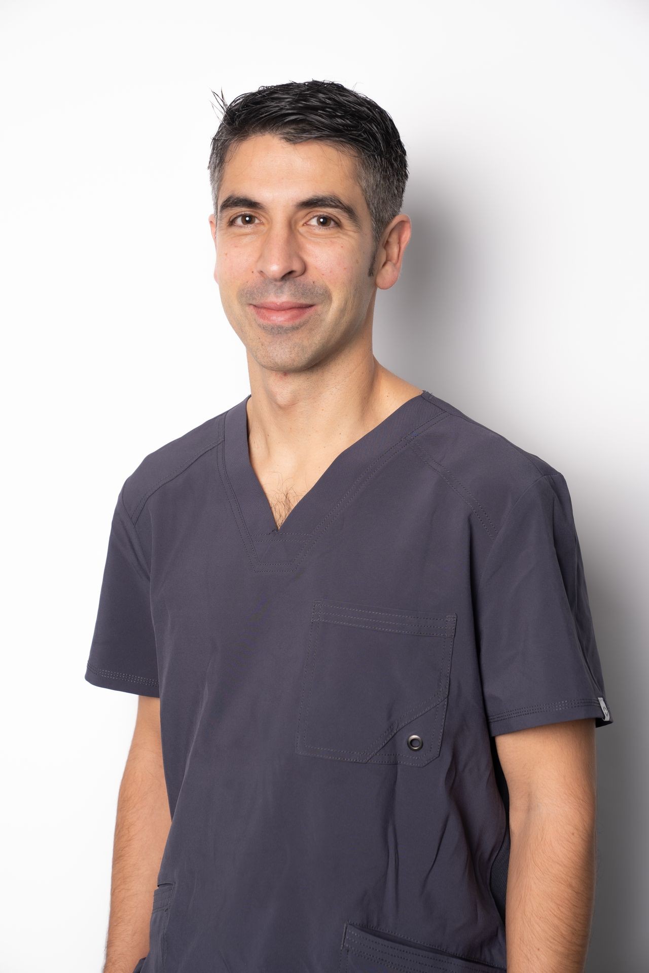 Person wearing a dark gray scrub top with short sleeves standing against a plain white background.