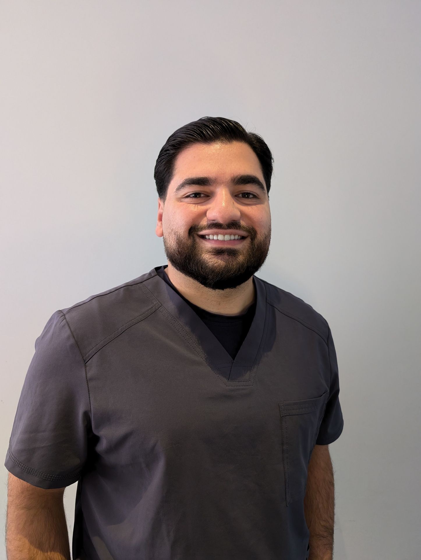 Person wearing a dark scrub shirt smiling against a light gray background.