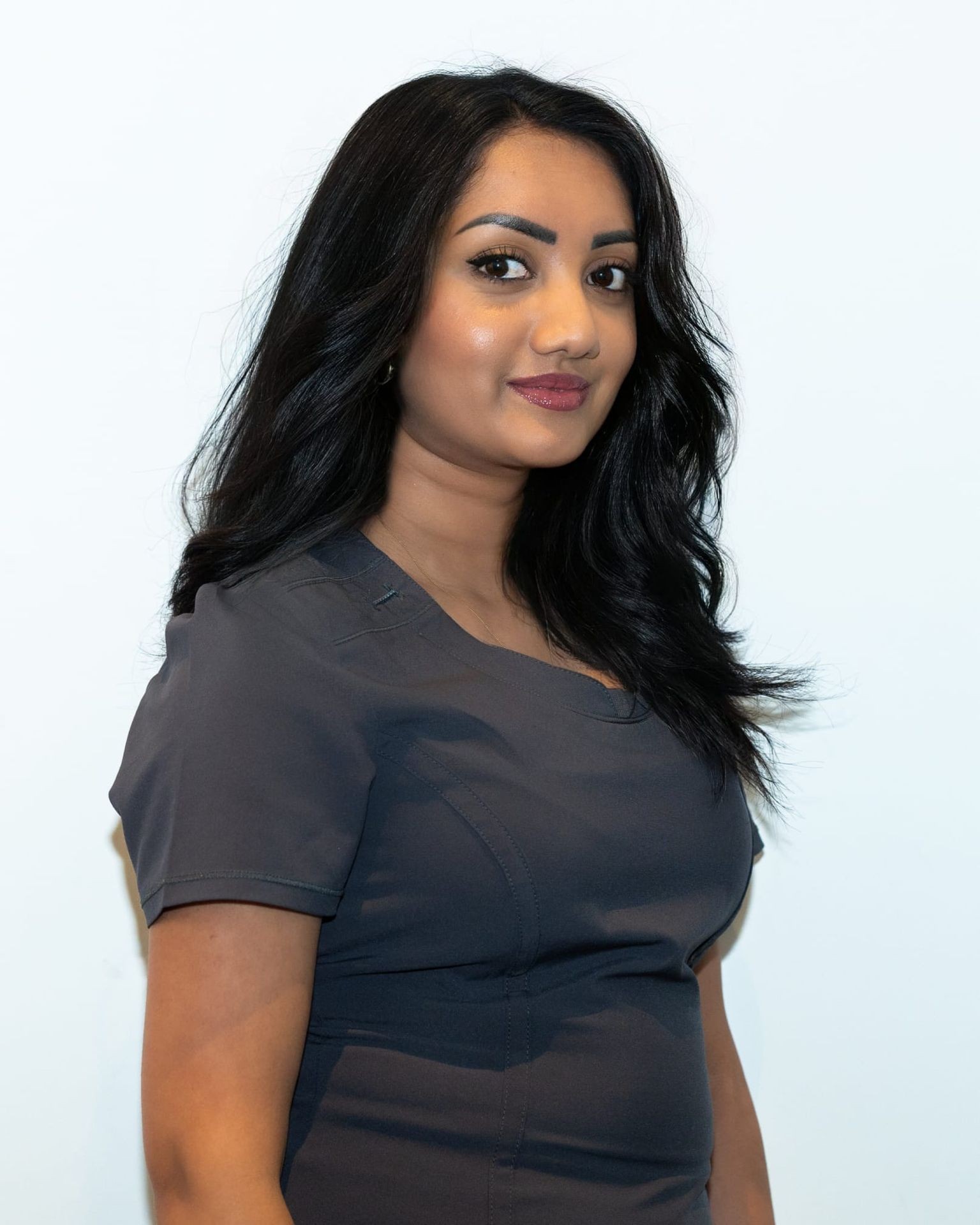 Woman with long black hair wearing a dark gray top standing in front of a plain white background.